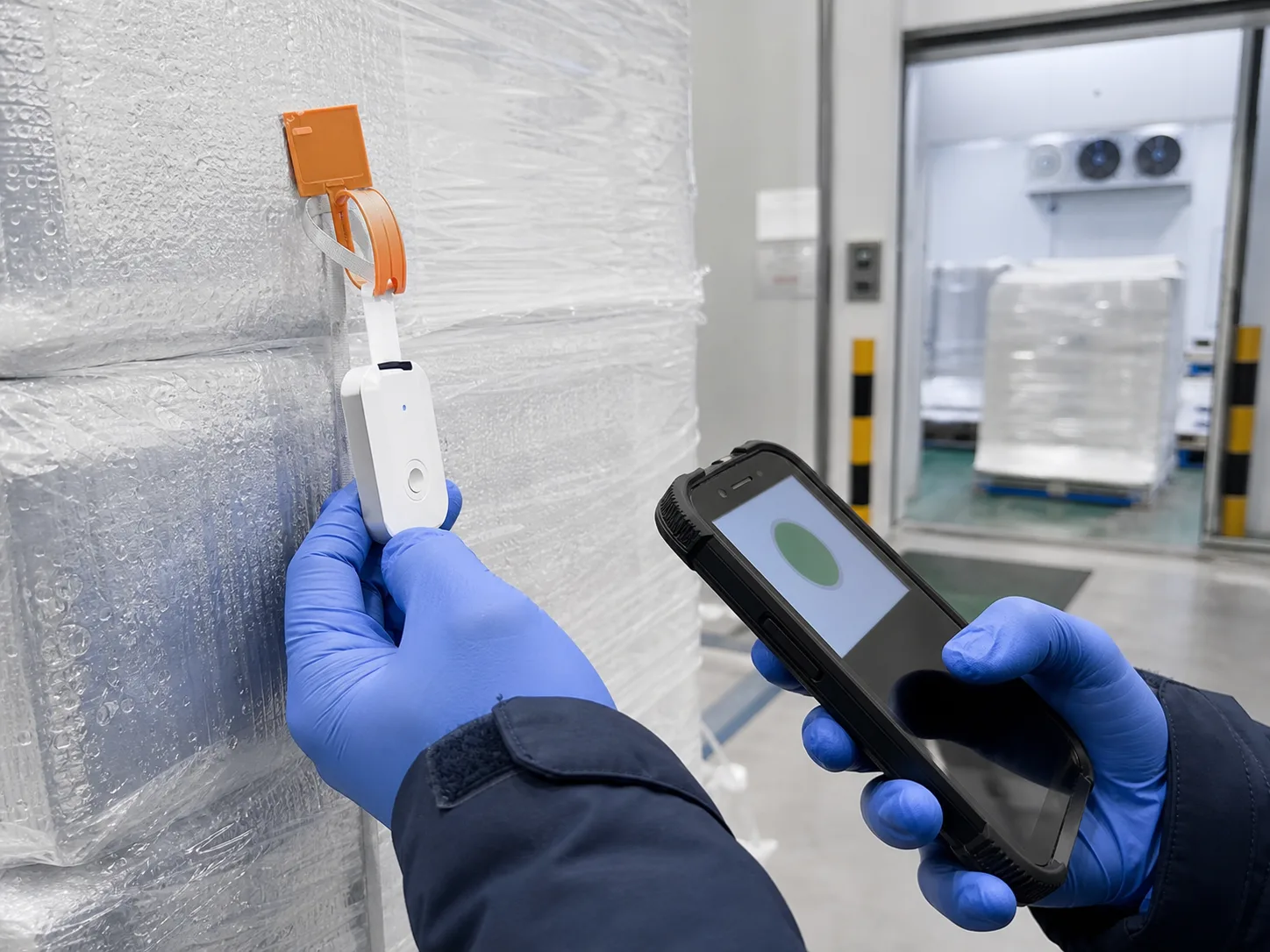 Gloved operator scanning a temperature logger attached to a sealed insulated pallet